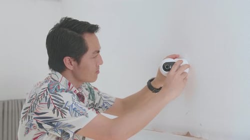 Young Man Installs Wireless Security Camera on Wall