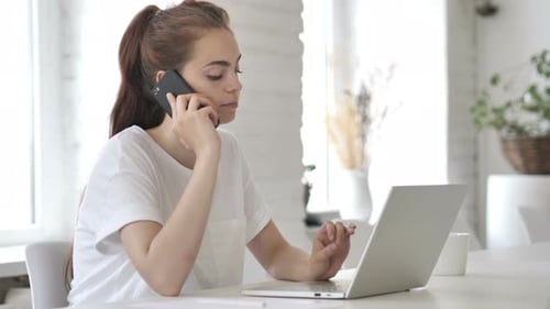 Woman Uses Laptop, Talks on Phone at Desk
