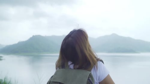 Hiker backpacker woman on hiking adventure feeling freedom walking in forest near lake in rainy day.
