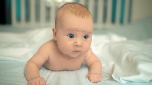 Cute Baby with Beautiful Blue Eyes Lying in White Bed