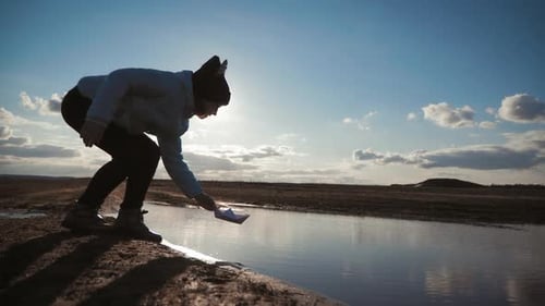 Cute Girl Plays with the Paper Ship in a Lake at Sunset Time. Child Dream and Travel Concept