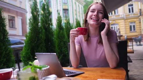 Young Woman Talking on the Phone in a Cafe on a Summer Terrace