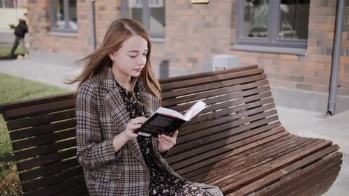 Young Woman Reading a Book on a Bench