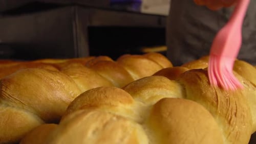 a cook combing melting butter with brush on baked bread