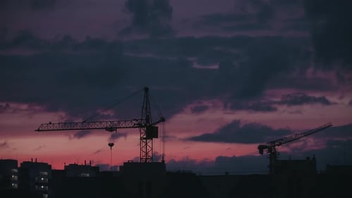 Construction Cranes Silhouetted Against Colorful Evening Sky