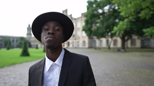 Stylish Man in Suit Adjusts Hat on Walkway