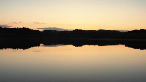 Flying shot over a reservoir and forest at sunset