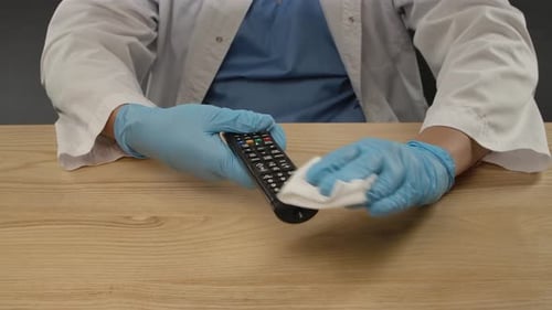 Hands in Gloves Cleaning a Remote Control