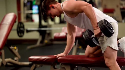 Closeup side view of young bodybuilder doing one arm dumbbell rows.