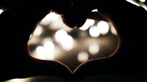 Hands Forming Heart Shape Against Bokeh Lights