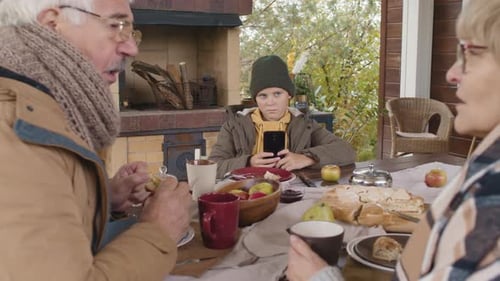 Boy Using Phone While Grandparents Chat Over Pie