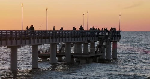 Silhouettes of People Walking on the Pier Against the Sunset. Local People Are Fishing, Tourists Are