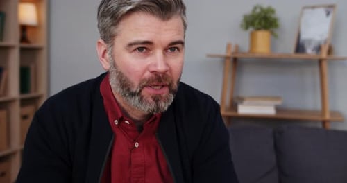 Close Up View of Mature Handsome Bearded Man Sitting on Couch and Talking