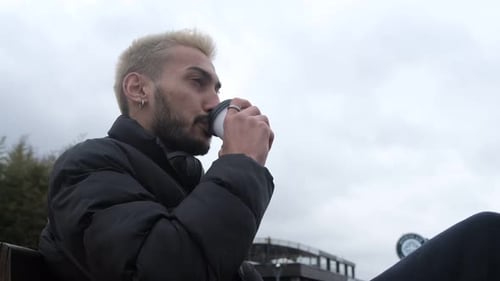 Man with Blond Hair Drinks Coffee Outdoors