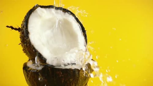 Water Pouring Over Coconut Halves on Yellow
