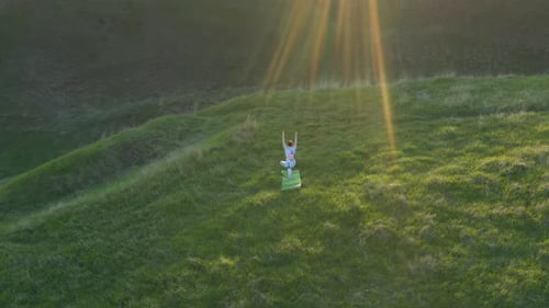 Woman Practicing Yoga on Grassy Hillside at Sunset
