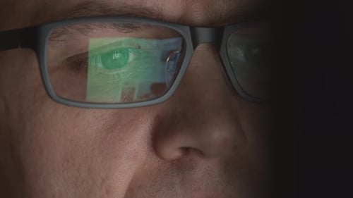 Reflexion von Scrollseiten in einer Brille eines jungen erwachsenen Mannes, der an einem Computer arbeitet