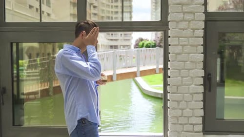 Man Stands Near Window and Rubs Neck