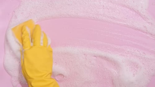 Hand in Yellow Glove Cleans Foamy Pink Surface