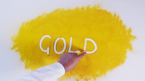 Hand Draws Gold in Yellow Powder