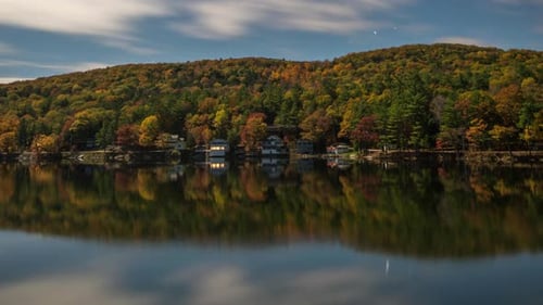 Timelapse of stars rotating across the night sky above autumn trees on a mountain range above a calm