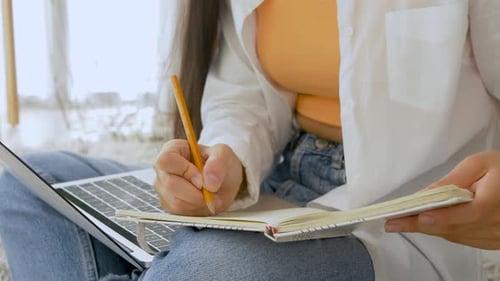 Woman Writes Notes While Working on Laptop