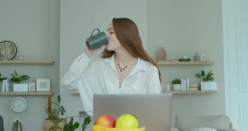 Woman Using Laptop and Drinking Beverage at Home
