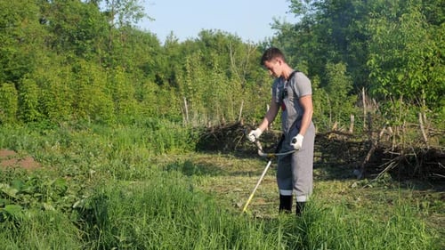 Man in Working Uniform Mows Grass with a Trimmer