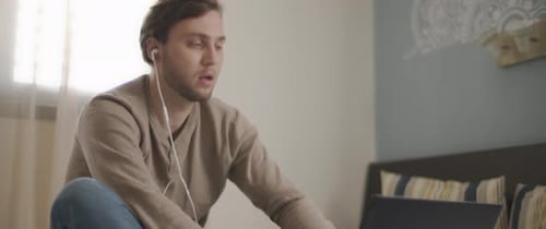 Young Adult Using Laptop with Earbuds Indoors