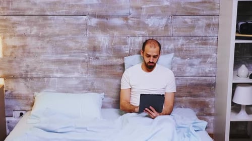 Man Using Tablet Device in Bed