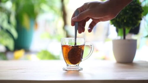 Eine erwachsene Hand rührt morgens ein Glas Tee auf dem Tisch.