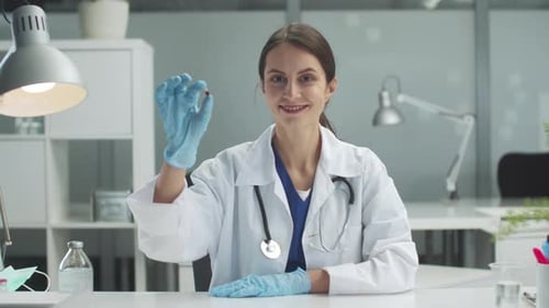A Young Female Medic Holds a Medicine Capsule in Her Hand and Examines It at the Clinic Table