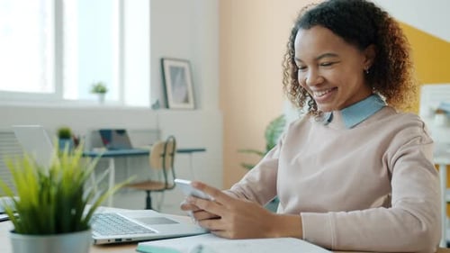 Mixed Race Girl Using Smartphone Touching Screen Smiling Sitting at Desk in Office Room