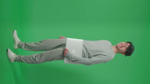 Full Body Of Side View Asian Man Holding Computer While Standing In Front Of Green Screen Background