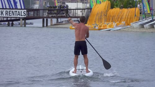 A man paddles his SUP stand-up paddleboard in a lake.