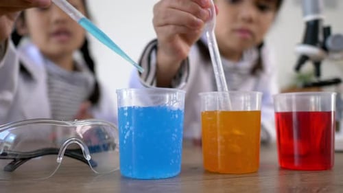 Girls Perform Chemistry Experiment with Pipettes and Beakers