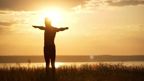 Silhouette of Young Sportive Man Practicing Yoga at Sunset