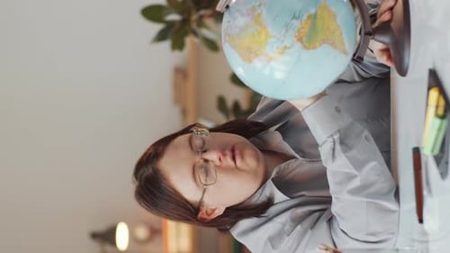 Woman Looking at Globe at Desk Indoors