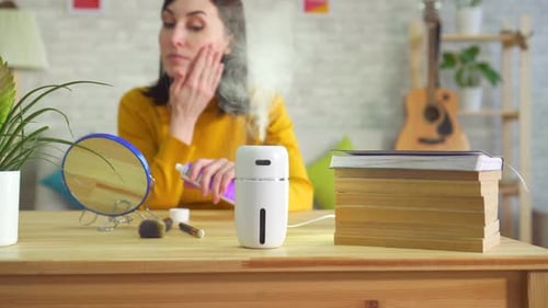Woman Applying Lotion to Face Next to Humidifier