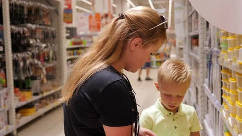 A Woman with a Young Son in a Supermarket is Choosing Plastic Dishes