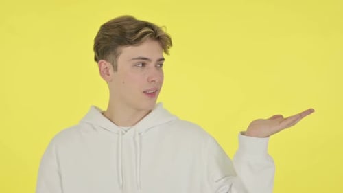 Smiling Man Holds Hand Out on Yellow Background