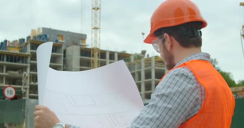 Nahaufnahme eines Ingenieurs mit Bauplan auf dem Hintergrund eines im Bau befindlichen Gebäudes.
Jung