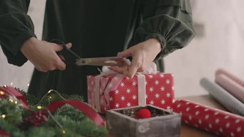 Person Wrapping Christmas Gift with Ribbon and Scissors