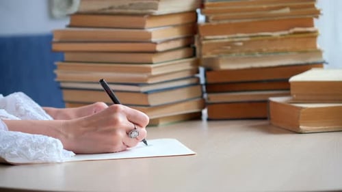 Hands Writing at Desk with Stack of Books