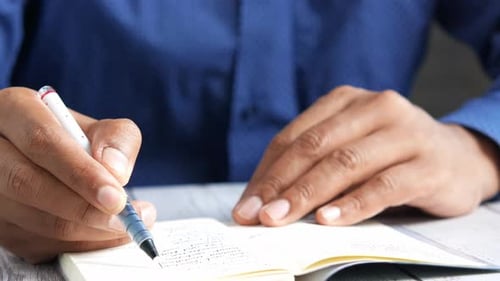 Man Hand Writing on Notepad While Sited