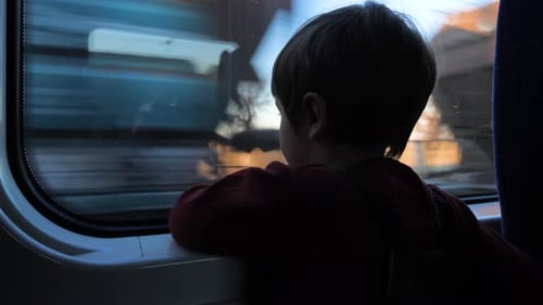 Child Looks Out Train Window at Passing Scenery