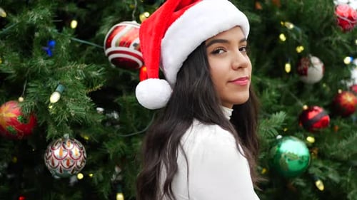 Festive Young Woman in Santa Hat by Christmas Tree