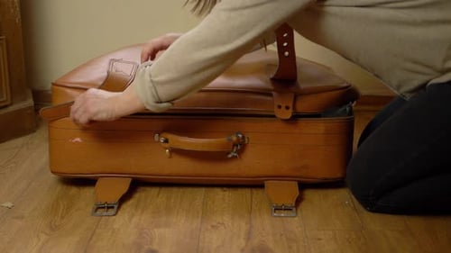 Person Closing Vintage Suitcase on Floor