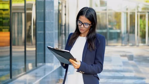 Young pretty female office clerk in suit and glasses checks documents, utility bills