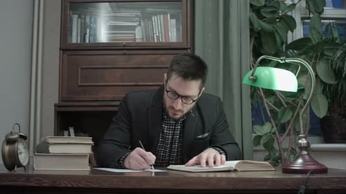 Konzentrierter männlicher Forscher liest Buch und macht Notizen am Schreibtisch